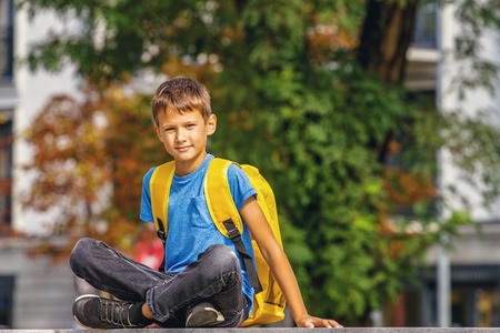 Cute smart boy with backpack sitting outdoors after school.の写真素材