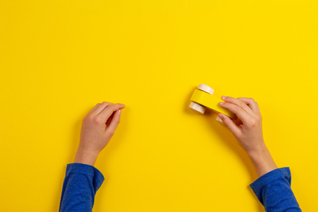 Child hands playing with wooden toy car on yellow background, top viewの写真素材