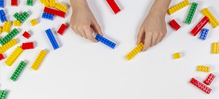 Kid hands playing with colorful building plastic bricks on white background