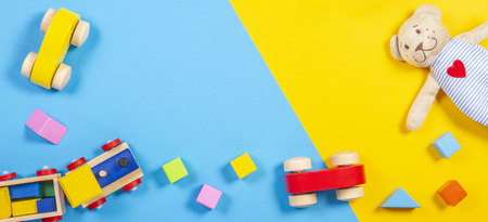 Baby kids toys frame with teddy bear, wooden toy train, cars, colorful bricks on yellow color background. Top view, flat layの写真素材