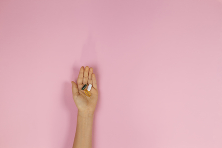Medicine capsules pills in kid hand on pink backgroundの写真素材