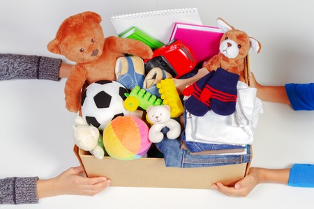 Donation concept. Kid hands with donate box with clothes, books, school supplies and toys, white...