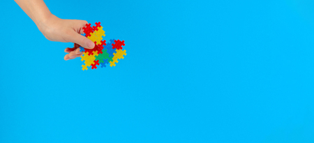 Child hand holding colorful heart on blue background. World autism awareness day conceptの写真素材