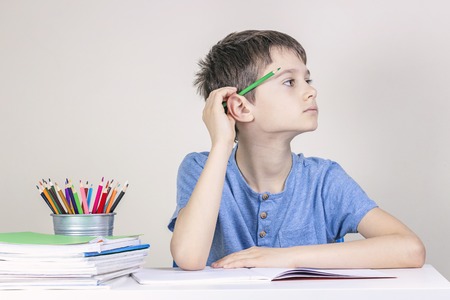 Kid doing homework at the table. Boy with pencil behind his ear thinking or dreaming and looking...