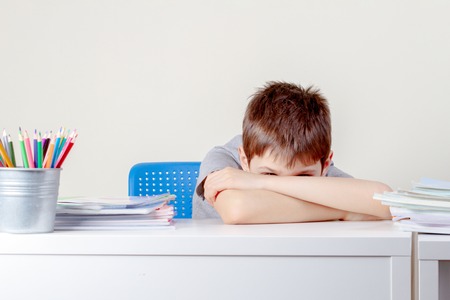Upset sad schoolboy with pile of school books and notebooksの写真素材