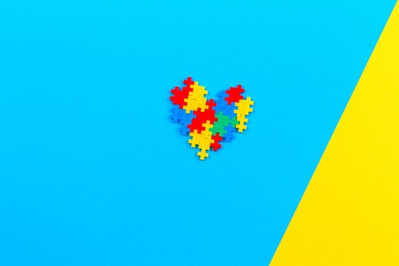 Top view on heart made of colorful plastic construction bricks on blue and yellow backgroundの写真素材