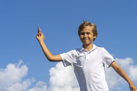 Happy kid playing with paper airplane against blue summer sky backgroundの写真素材