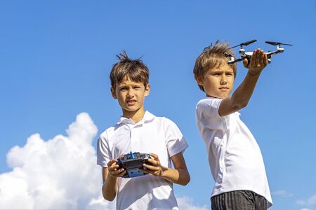 Boys playing with drone in summer day outdoors against blue skyの写真素材