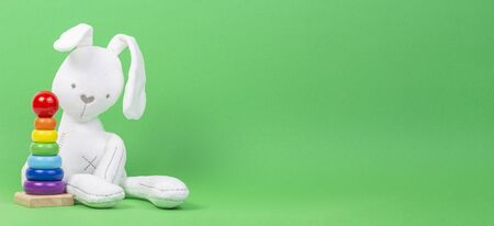 White plush toy rabbit with wooden baby stacking rings pyramid on light green backgroundの写真素材