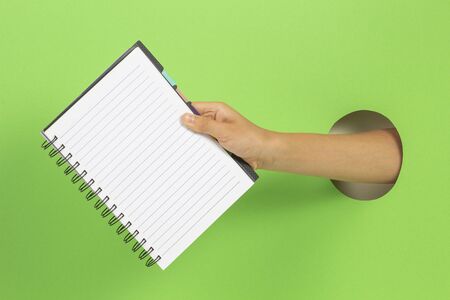 Kid holding open spiral notebook in hand through hole on light green backgroundの写真素材