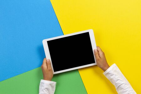 Kid hands with tablet computer on yellow, blue and green backgroundの写真素材