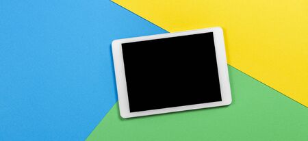 Digital tablet computer on light blue, green and yellow background. Top view