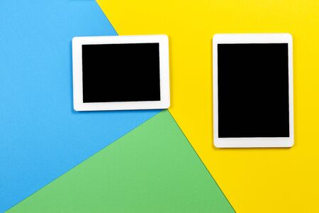 Two digital tablet computers on light blue, green and yellow background. Top viewの写真素材