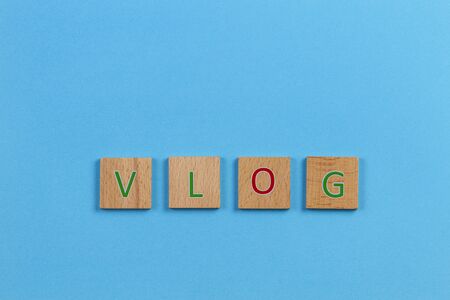 The word VLOG, spelt with wooden letter tiles over blue background. Top viewの写真素材