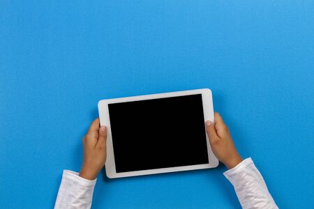 Kid hand holding white tablet computer on light blue backgroundの写真素材