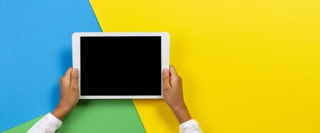 Kid hands with tablet computer on yellow, blue and green backgroundの写真素材