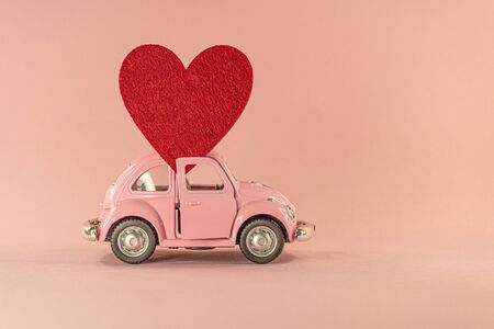 Little retro toy model car with red heart on pastel pink background. Love, friendship, valentines day, delivery, donation conceptの写真素材