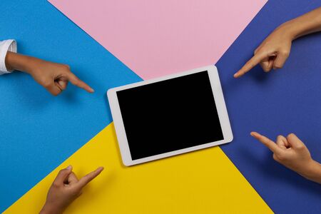Kids hands pointing fingers to blank tablet computer on colorful background