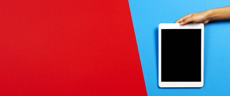 Kid hand with tablet computer on red and light blue background