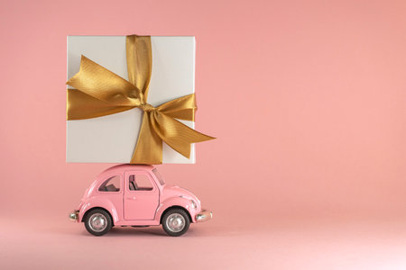 Little retro toy model car with present gift box on pastel pink background. Christmas, birthday, valentines day, delivery conceptのeditorial素材