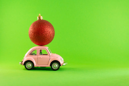 Vilnius, Lithuania - September 09, 2019: Pink retro toy model car with small red Christmas tree decoration bauble on green backgroundのeditorial素材