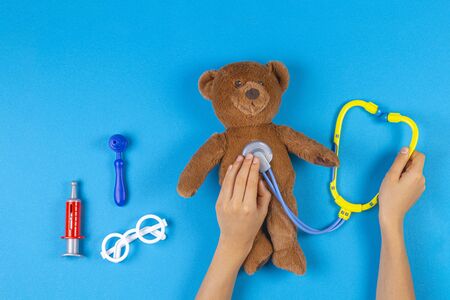 Kid hands with toy stethoscope, teddy bear and toy medicine tools on light blue background. Top viewの写真素材