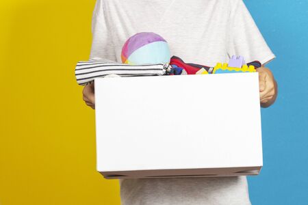 Donation concept. Kid hands holding donate box with books, clothes and toys.