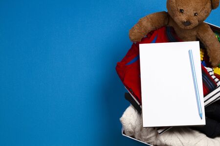 Donation box with clothing, books, children toys with blank notebook page and pencil on blue...