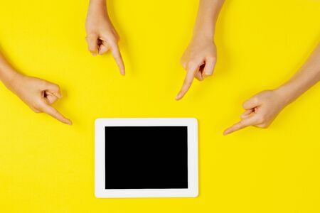 Many kids hands pointing to tablet computer on yellow backgroundの写真素材