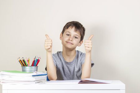 Happy boy making homework tasks and showing thumbs up sign