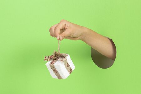 Hand through hole on light green background holding present gift box decoration