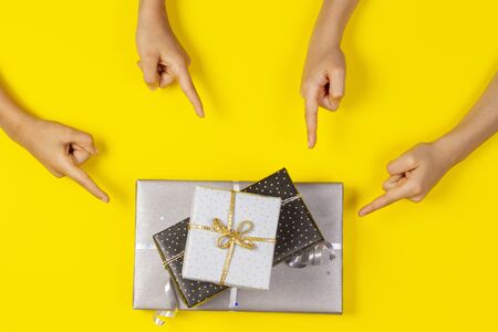 Many hands pointing to wrapped present gift boxes on yellow background. Top viewの写真素材