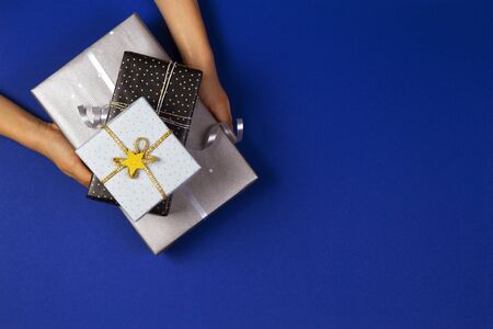 Hands holding presents wrapped in gift paper on navy blue background. Christmas, New Year, holidays...
