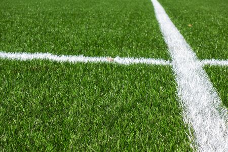 Green synthetic artificial grass soccer sports field with white stripe lines.