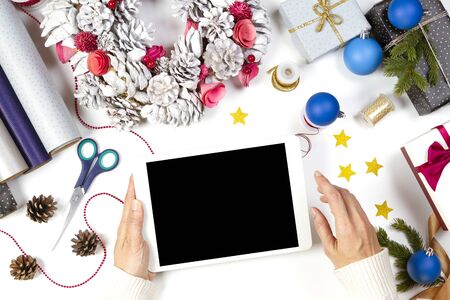 Christmas shopping and present wrapping. Top view of female hands holding a tablet computer over white table with Christmas present gift boxes, Xmas tree branchの写真素材