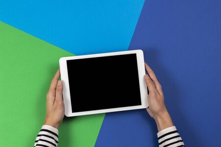 Female hands with digital tablet computer on navy blue and light green background. Top viewの写真素材