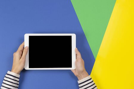 Female hands with digital tablet computer on blue yellow and light green background. Top viewの写真素材