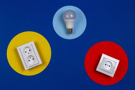 One light lamp bulb and electrical power sockets on yellow red and navy blue background.