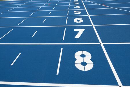 Blue running treadmill track with lane numbers in stadium outdoors.の写真素材