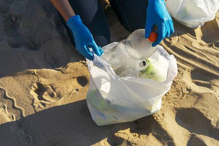 Cleaning city beach from plastic trash. Woman hands picking up plastic bottle trash from the beach...