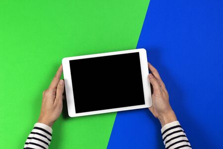Woman hands holding digital tablet computer on green and blue background