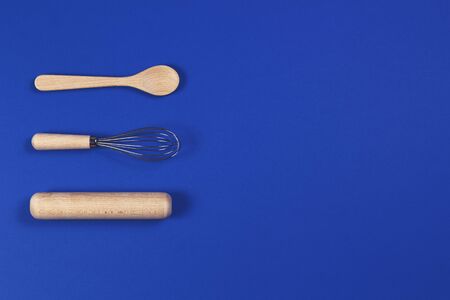 Bakeware. Wooden spoon, rolling pin and balloon whisk on blue background. Top view