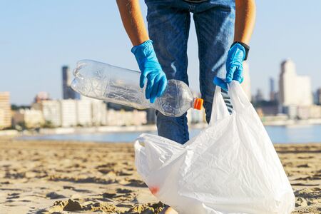 Clean beach from plastic. Hand picking up plastic bottle trash from the beach and putting into...