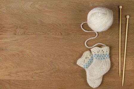 Knitting background. Wooden knitting needles, ball of yarn and small wool knitted socks on wooden backgroundの写真素材