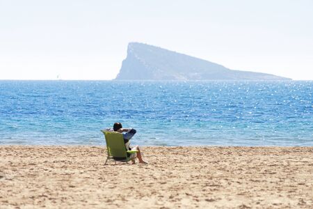 Unrecognizable man sitting on a beach chair on empty Poniente beach by Mediterranean sea in Benidormの写真素材