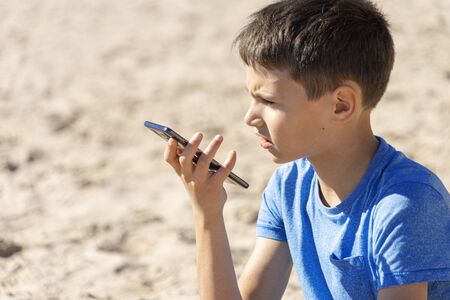 Teenager boy using a smart phone voice recognition function online, using cell phone to send a voice...