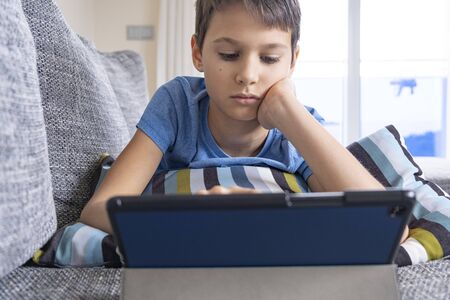 Boy lying on sofa with digital tablet computer at home. Technology, ditance education, online...