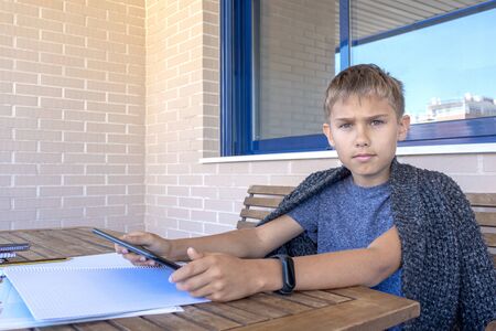 Child with tablet computer and books notebooks doing homework in balcony. School, online learning,...