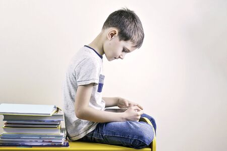 Boy with tablet computer and stack of books near him. Online learning, home school, technology, education for kids.の写真素材