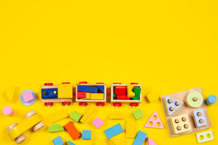 Baby kids toys background. Wooden train, educational stacking color recognition puzzle toy and colorful blocks on yellow background. Top viewの写真素材